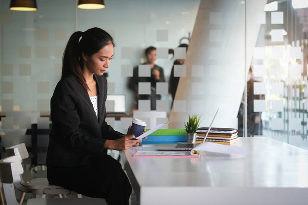 Femme d'affaires lisant des informations sur la paperasserie et utilisant un ordinateur portable travaillant sur bureau. - Photo, image