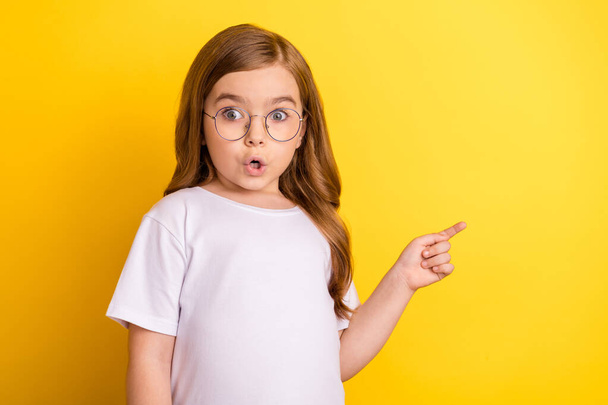 Photo of young little girl amazed shocked omg wow point finger empty space advertise direct isolated over yellow color background - Foto, Bild