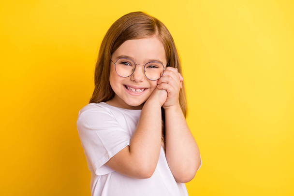 Photo of young little pretty girl happy positive smile hands touch cheeks isolated over yellow color background - Foto, imagen
