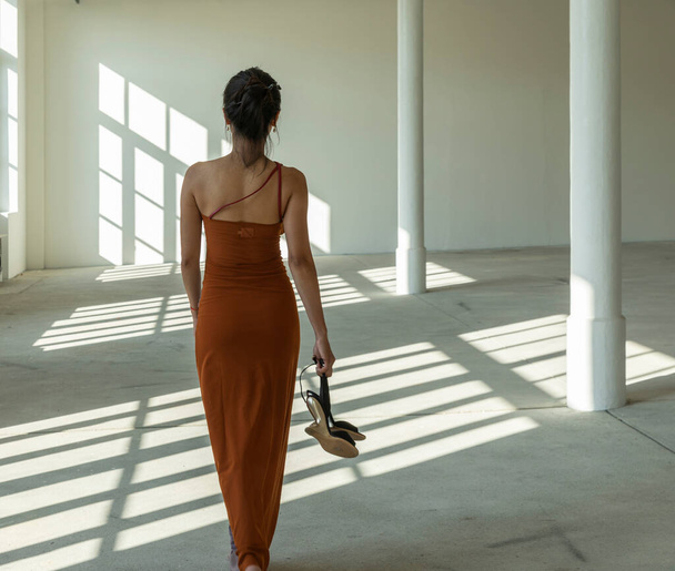 Asian girl in traditional Chinese dress walks barefoot sensually in an empty industrial building illuminated by natural sunlight. Copy space  - Фото, изображение