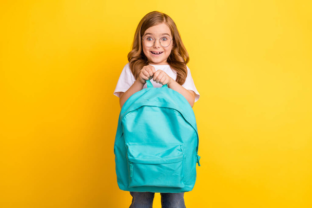 Photo of cheerful impressed school girl wear white t-shirt spectacles holding rucksack smiling isolated yellow color background - Foto, Imagem