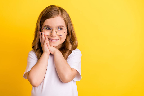 Photo of impressed pretty school girl wear white t-shirt spectacles smiling looking empty space isolated yellow color background - Photo, image