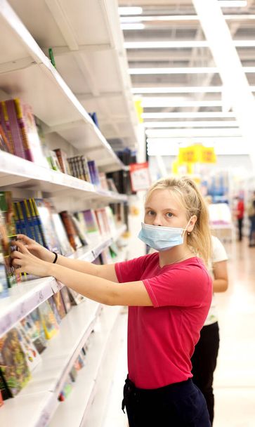 Portrait of   young female student choosing office supplies in   medical mask - Φωτογραφία, εικόνα