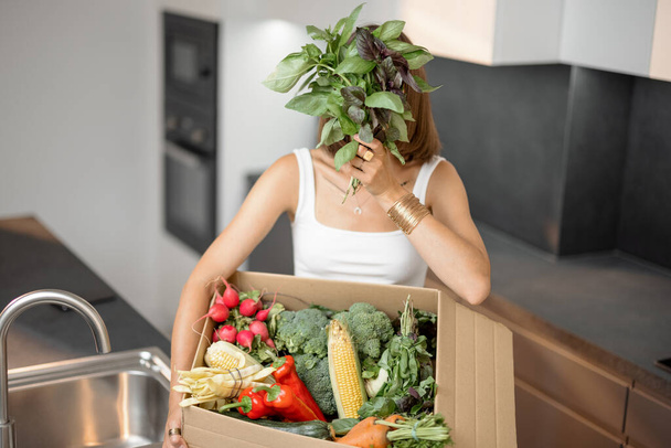 Nő friss zöldségekkel kartondobozba csomagolva a konyhában - Fotó, kép
