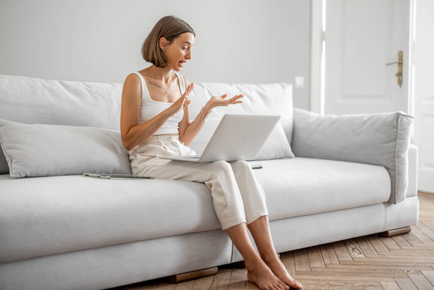 Γυναίκα μιλάει στο διαδίκτυο, κάθεται στον καναπέ στο σπίτι - Φωτογραφία, εικόνα