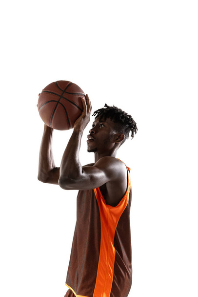 Portrait vertical. Jeune homme africain, joueur de basket pratiquant avec balle isolé sur fond de studio blanc. - Photo, image