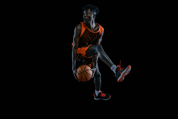 Jogador profissional de basquete africano praticando com bola isolada sobre fundo escuro estúdio. - Foto, Imagem