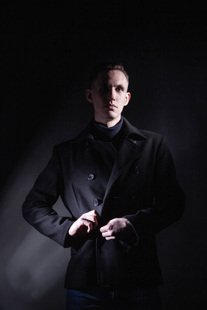 Stijlvolle man in zwarte jas in donkere studio - Foto, afbeelding