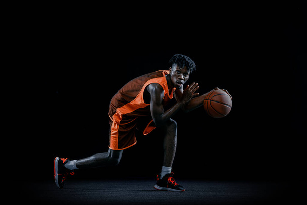 Professional african basketball player practicing with ball isolated over dark studio background. - Fotoğraf, Görsel