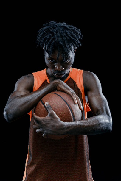 Zbliżenie. Profesjonalny afrykański koszykarz pozowanie z piłką izolowane nad ciemnym tle studio. - Zdjęcie, obraz