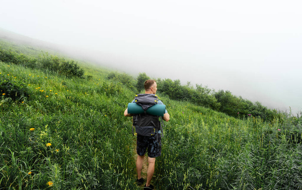 Hiker with big traveling rucksack moving up on the mountain trail among the tall grass. - Foto, immagini