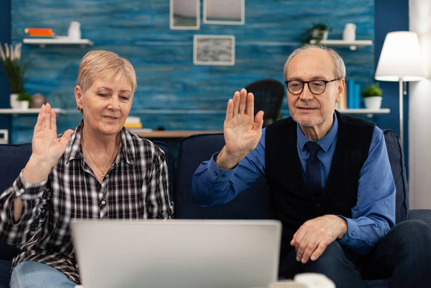 Веселая пожилая пара в гостиной машет веб-камерой - Фото, изображение