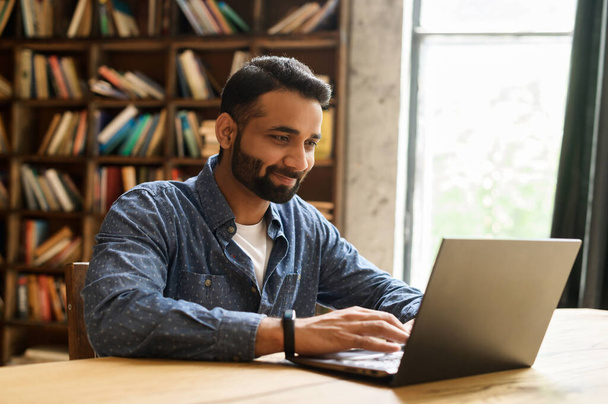 Positive Indian male freelancer looks at the laptop monitor - Fotó, kép