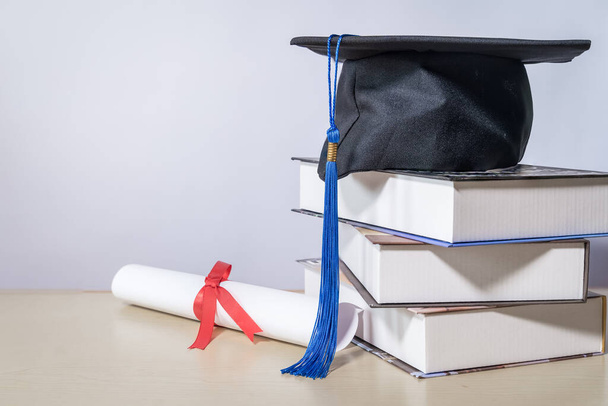 Стокова фотографія випускної шапки з книжками та сертифікатом диплома ізольовані на дерев'яному столі на білому тлі з негативним місцем для копіювання, щоб додати текст. Концепція випуску освіти
 - Фото, зображення