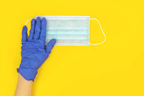 Dotor in medische handschoen houden gezichtsmasker op een gele tafel achtergrond, bovenaanzicht  - Foto, afbeelding