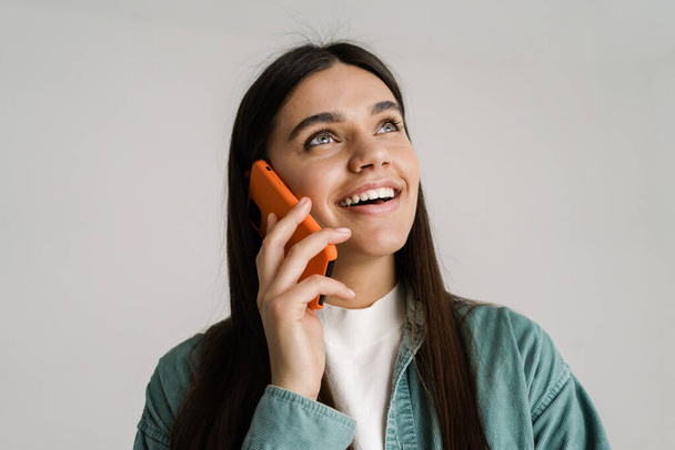 Young brunette woman smiling while talking on mobile phone isolated over white background - Φωτογραφία, εικόνα