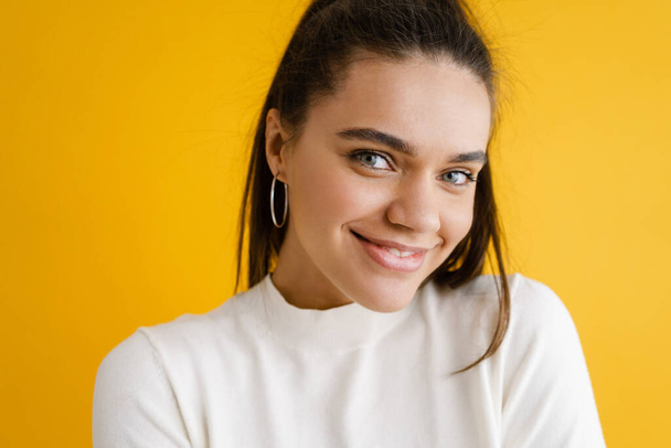 Young brunette woman smiling and looking at camera isolated over yellow background - Fotó, kép