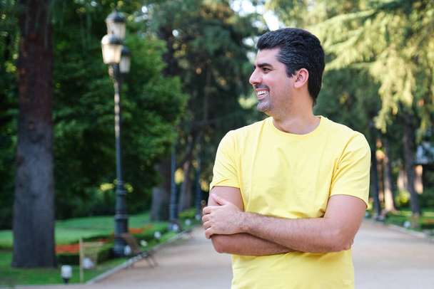 Muotokuva miehestä, joka hymyilee ja katsoo sivusta, seisoo puistossa. - Valokuva, kuva