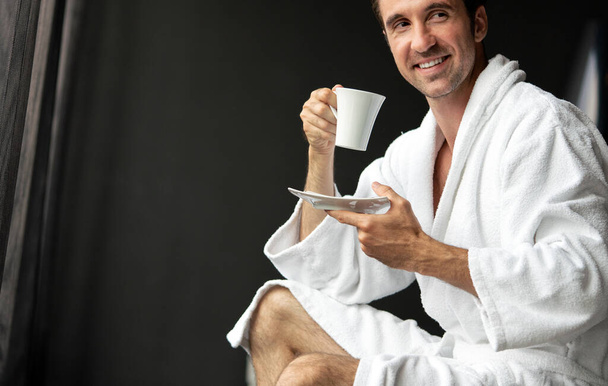 Male in bathrobe relaxing while drinking tea, coffee - Photo, Image
