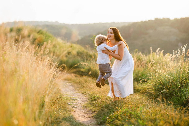 Glückliche Mutter nimmt ihren Sohn beim Spazierengehen in der Natur in den Arm - Foto, Bild