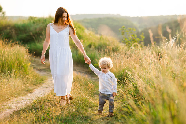 Η μαμά και ο γιος περπατούν κρατώντας τα χέρια στο καλοκαιρινό χωράφι - Φωτογραφία, εικόνα