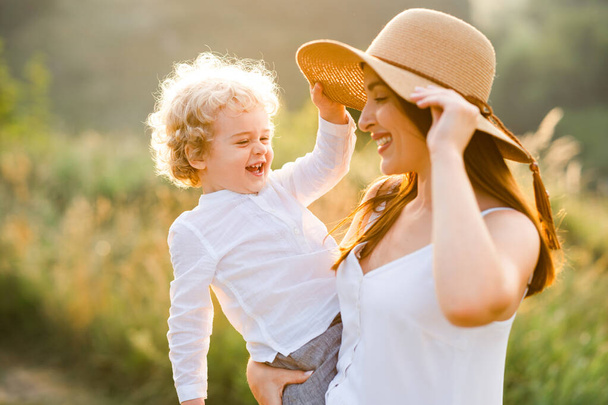 Pretty woman in straw hat holds a boy in her arms - Foto, afbeelding