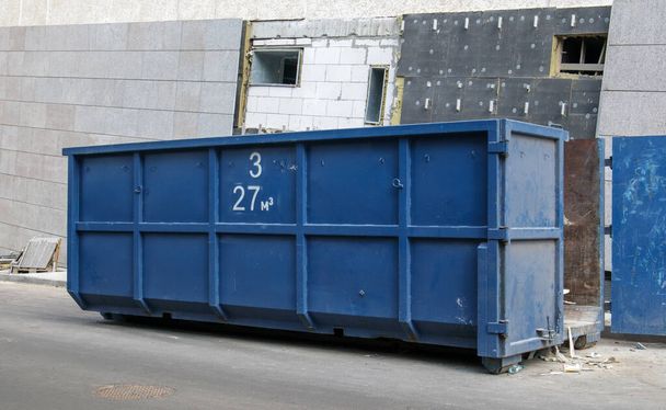 Metal durable blue industrial trash bin for outdoor trash at construction site. Large waste basket for household or industrial waste. A pile of waste - Photo, Image