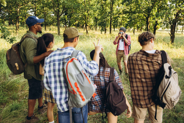 Bir grup arkadaş, genç erkekler ve kadınlar yaz ormanlarında piknik yaparken, çayırda yürüyorlar. Yaşam tarzı, arkadaşlık., - Fotoğraf, Görsel