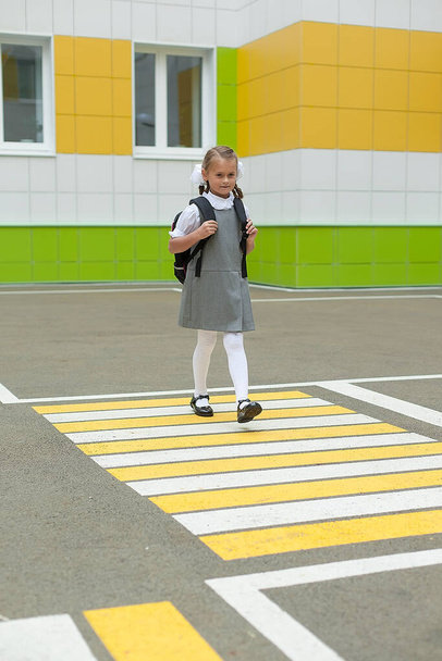 de volta à escola. Uma menina com mochilas escolares vai à escola, sorri e olha para a câmera. Uma criança caminha perto do jardim da escola. Ano Novo de estudantes - Foto, Imagem