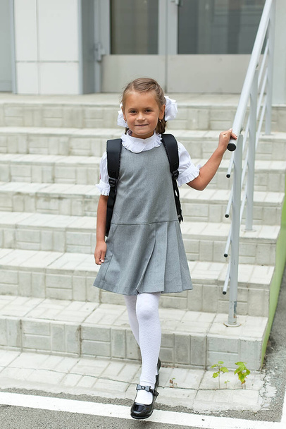 a schoolgirl girl on a school background with a backpack, smiling, with long hair, in a school uniform is going to study as an excellent student at the beginning of the school year. September 1. - Photo, Image