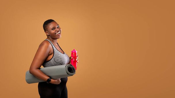 negro mujer posando con estera y agua en estudio - Foto, Imagen