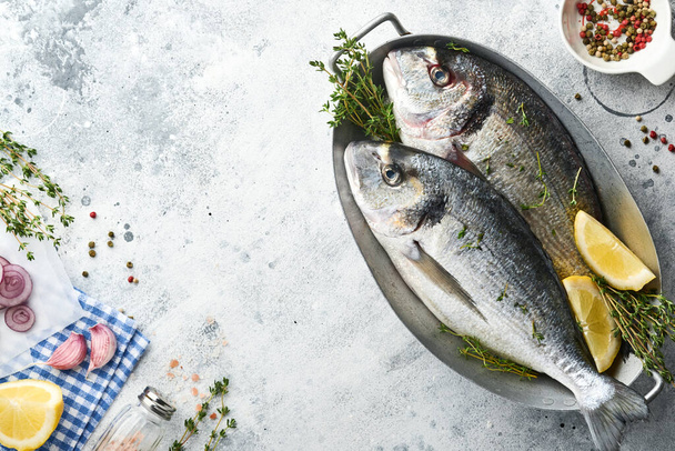 Raw dorado fresh fish or sea bream with ingredients for making lemon, thyme, garlic, cherry tomato and salt on light grey slate, stone or concrete background. Top view with copy space. - Фото, изображение