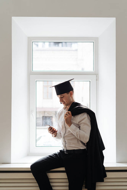 Kaukaski młody człowiek czuje się bardzo podekscytowany otrzymaniem dyplomu licencjata za pomocą telefonu - Zdjęcie, obraz