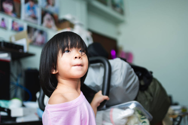 A cute Asian girl looks up at the TV in the house at close range. Children wear pink t-shirts aged 4-5 years. Child have hair covering their eyes. - Photo, Image