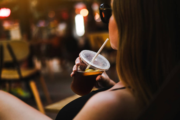 Frau trinkt einen Cocktail auf einem Sommerfest in einem Restaurant in Großaufnahme. Frau hält kaltes Getränk bei sich - Foto, Bild