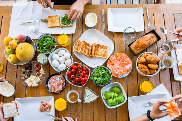 Food on the table. Breakfast on the terrace with the family. Friends are eating at the table. World Food Day Healthy Food Table Top View Party Birthday Lots of food for breakfast. Buffet. Avocado, salmon, cheese, cherry. Family eats - Foto, imagen