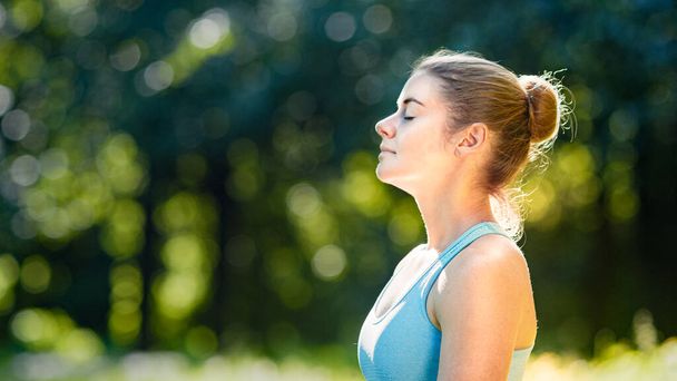 Mladá žena sportovec s vlasy bun uvolňuje po cvičení a medituje stojící v jóga póze - Fotografie, Obrázek