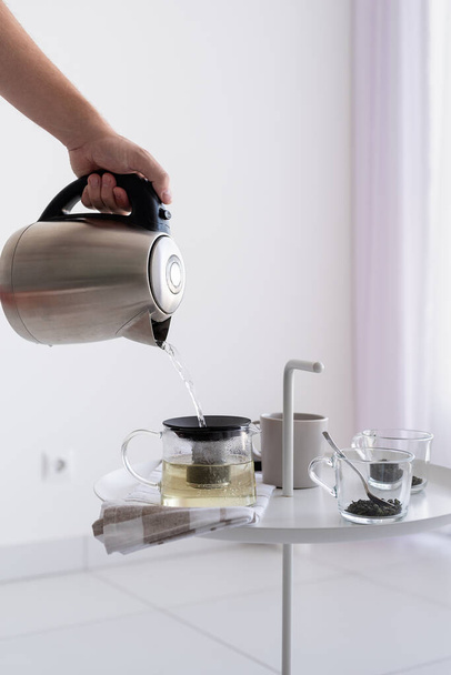 お茶を作る。コーヒーテーブルと男の手のケトルを閉じ、お茶を作るためのお湯を注ぐ - 写真・画像