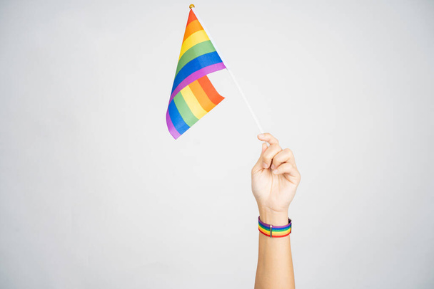 LGBT έννοια. Κρατώντας μια σημαία ουράνιο τόξο σε λευκό φόντο. Μεμονωμένο φόντο. - Φωτογραφία, εικόνα