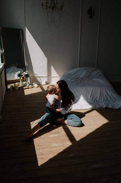 elegante mamma e bambina sono seduti su un pavimento di legno nei raggi di luce - Foto, immagini