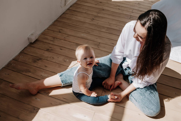 eine brünette Mutter und ein kleines Mädchen sitzen auf einem Holzboden in den Lichtstrahlen - Foto, Bild