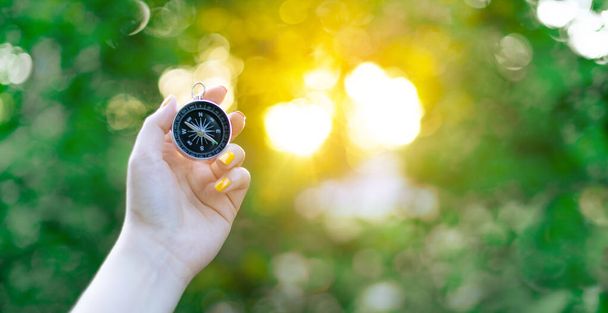 Hand with compass on green blurred background with sun glare at sunset sky - 写真・画像