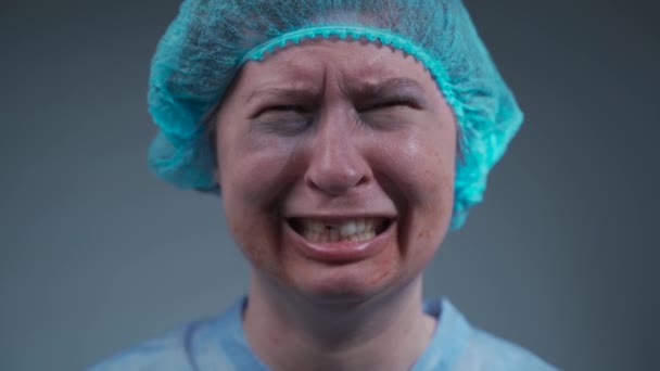 Muotokuva mustelma naisesta lääketieteellisissä vaatteissa hakattuna kasvoihin ja hampaisiin sairaalassa, katsoen kameraan ja itkien, perheväkivallan uhri. Stressaava nainen onnettomuuden jälkeen klinikalla itkeä - Materiaali, video