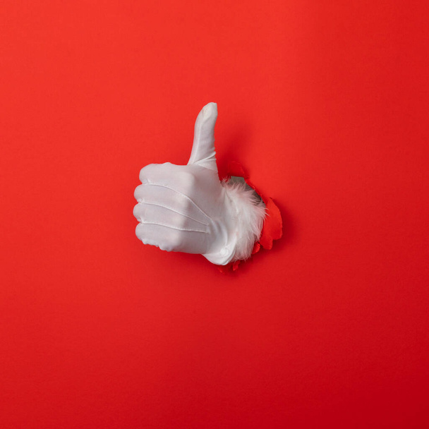 Santa Claus hand thumbs up through a hole in red paper background - Foto, Bild