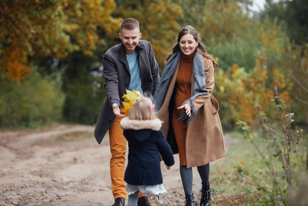 Vater Tochter und schwangere Mutter spazieren durch Herbstpark junge glückliche Familie - Foto, Bild