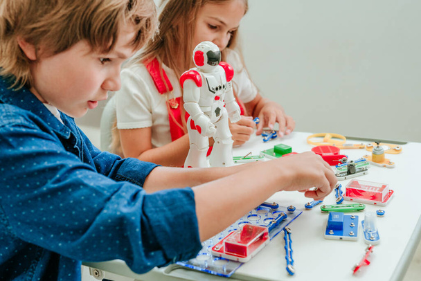 Мальчик-подросток и девочка играют с роботом во время урока в классе. - Фото, изображение