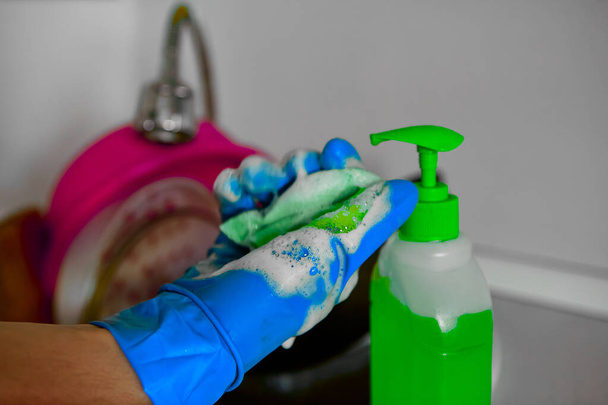 Close-up of hands in rubber gloves holding a sponge and squeezing out dishwashing liquid. Green detergent. - Photo, Image