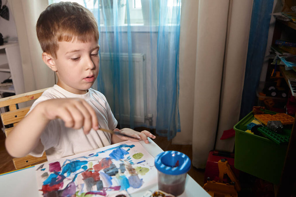 A boy draws with paints at a table in his room - Photo, Image