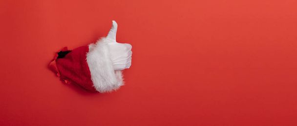 Santa Claus hand thumbs up through a hole in red paper background - Foto, immagini
