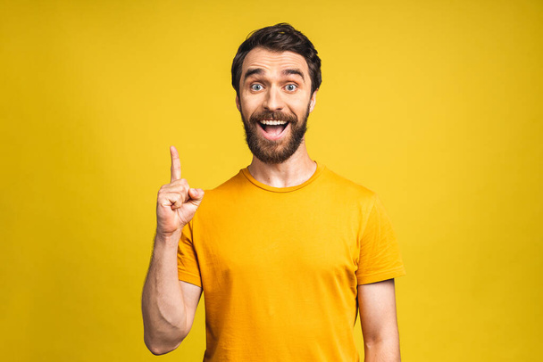 Look over there! Happy young bearded handsome man in casual pointing away up and smiling while standing isolated over yellow background. - Zdjęcie, obraz